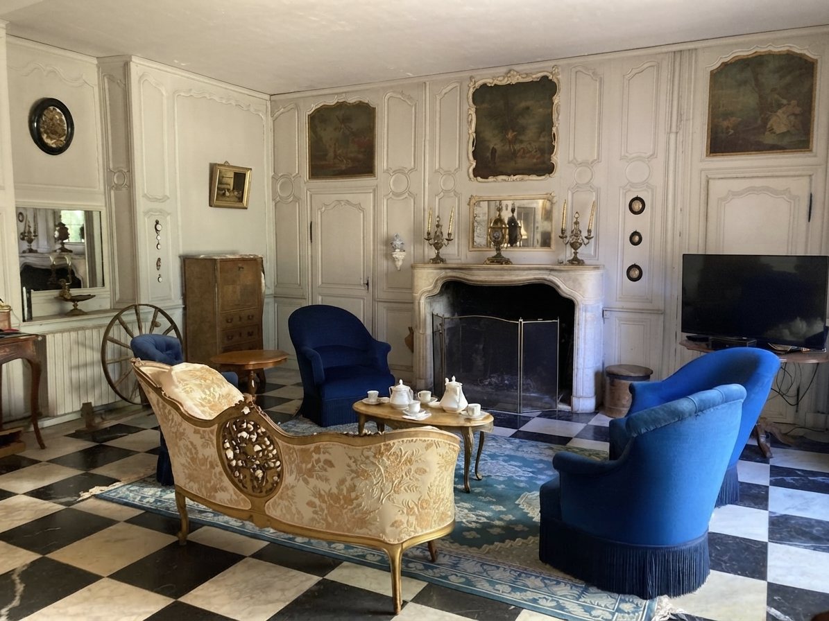Le salon : boiseries blanches, cheminée, fauteuils bleus et sol en damier noir et blanc